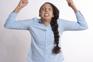 Very poor image of a woman in a blue shirt raising her hands in exasperation.