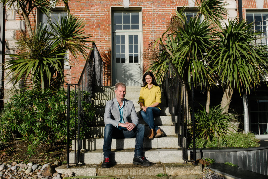 A picture of Martin Philp and Gargi Philp from Coast Copywriting, which provides SEO in Cornwasll, in front of a red brick building flanked by Australian palms