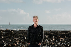 Penzance copywriter Martin Philp in black short with ocean background.